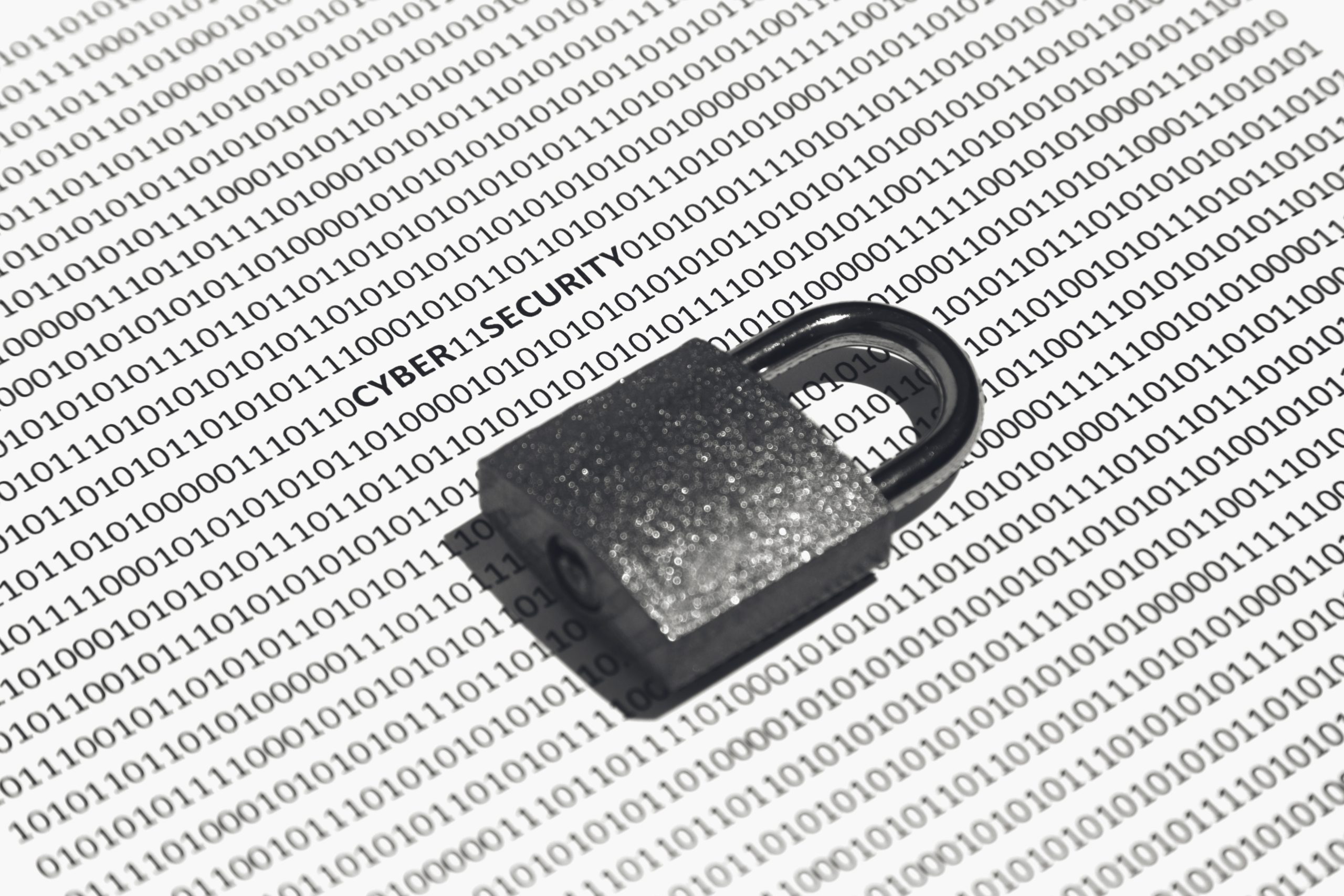 Nahaufnahme eines Schlosses auf einer weißen Fläche, auf der Cybersicherheit, Einsen und Nullen stehen